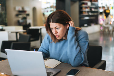 Mid adult woman using mobile phone while sitting on table