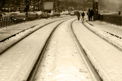 People walking on snow covered railroad tracks in city during winter