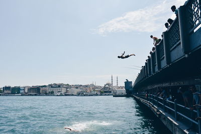 Men jumping in river by people on bridge