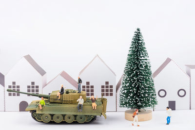 Close-up of figurines with christmas tree and toy armored vehicle against white background