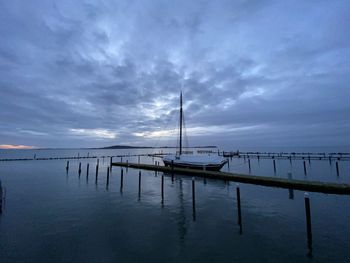 Sailboats moored on pier by sea against sky