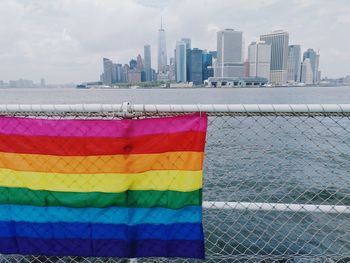 Rainbow flag hanging on railing against river in city