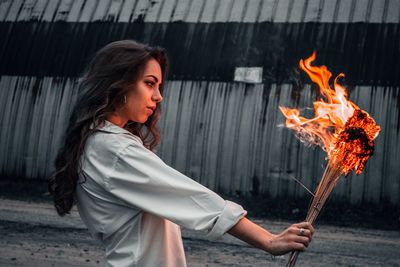 Side view of young woman holding burning outdoors
