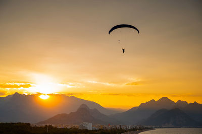 Silhouette person paragliding against sky during sunset