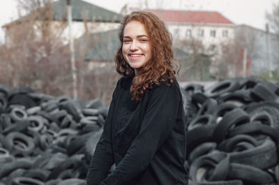 Cheerful curly-haired girl standing against a landfill of used car tires