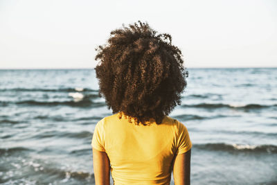 Afro woman looking at horizon from beach on sunny day