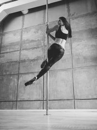 Full length of sensuous woman practicing pole dance in studio