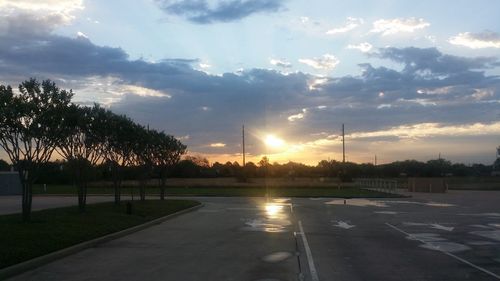 Road by trees against sky during sunset