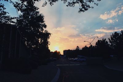 Road by silhouette trees against sky during sunset