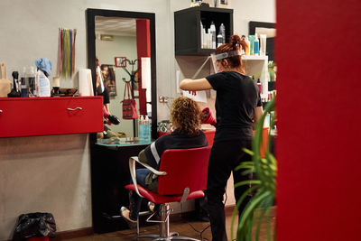 Hairdresser with a face shield dries her client's hair in her salon