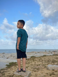 Side view of boy standing at beach against sky