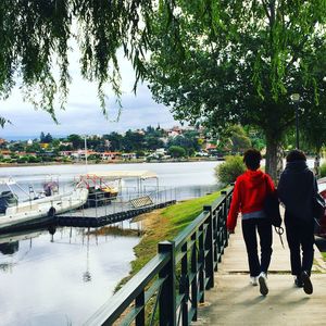 Rear view of people walking on footpath by river at park