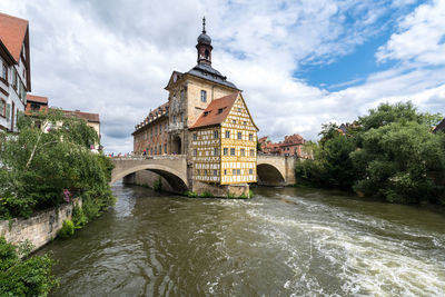 Arch bridge over river amidst buildings against sky