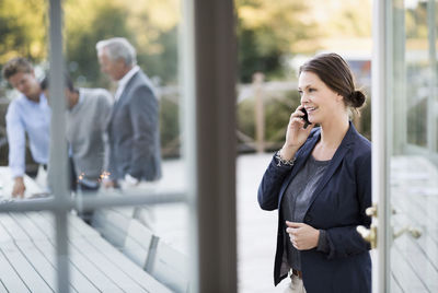 Businesswoman using mobile phone at patio with colleagues working in background