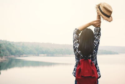 Rear view of young woman standing against lake