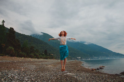 Full length of happy woman standing on mountain against sky