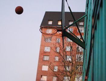 Low angle view of basketball in mid-air against building