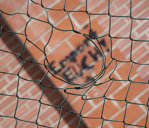 Text on wall seen through damaged chainlink fence