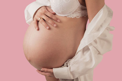 Midsection of pregnant woman touching belly against pink background