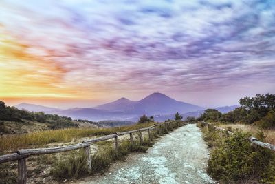 Empty road amidst field against sky during sunset