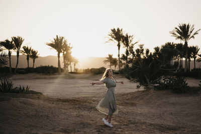 Young woman spinning with arms outstretched at beach during sunset