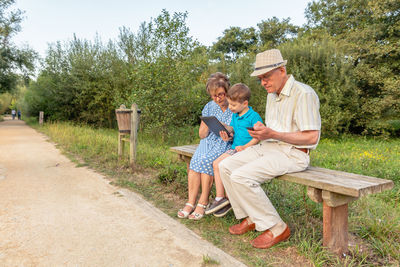 Grandson teaching digital tablet to grandmother while grandfather using mobile phone in public park