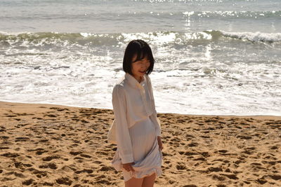 Young woman standing at beach during sunny day