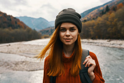 Portrait of young woman in hat standing against water