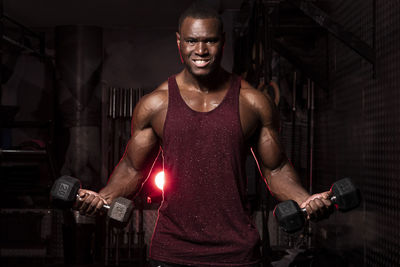 Portrait of young man exercising with dumbbells while standing in gym