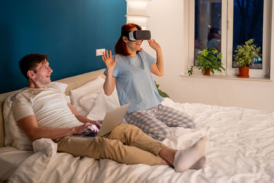 Side view of woman using mobile phone while sitting on bed at home