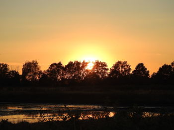 Silhouette trees by lake against sky during sunset