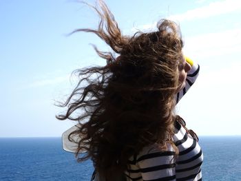 Side view of woman with tousled hair standing by sea against sky during sunny day