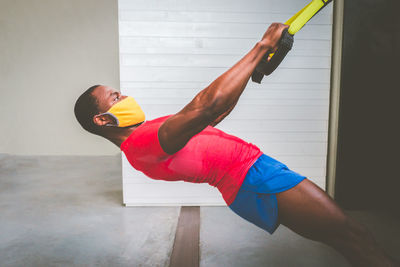 Side view of man wearing mask exercising against wall