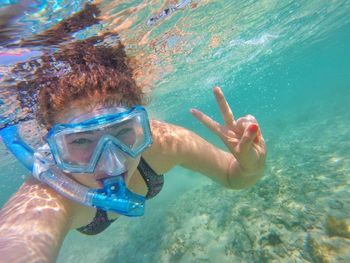 Portrait of woman gesturing peace sign while snorkeling in sea