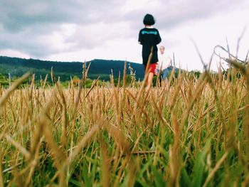 Father and daughter on field against cloudy sky