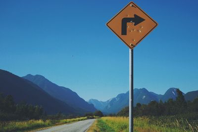 Road sign by mountains against clear blue sky