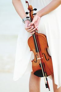 Midsection of woman holding violin at beach