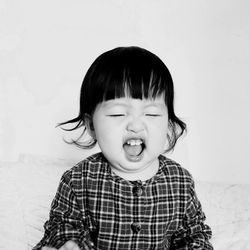 Close-up of cute baby girl with eyes closed and mouth open against white background