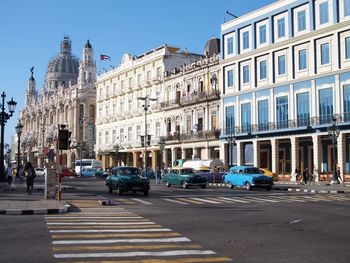 Cars on city street by buildings against sky