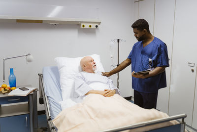 Male nurse with hand on shoulder of senior patient lying in hospital