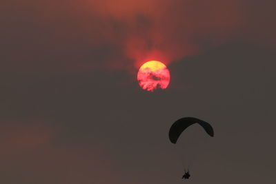 Low angle view of person paragliding against sky at sunset