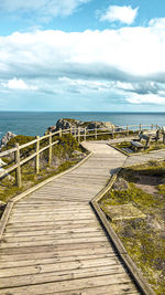 Footpath leading towards sea against sky