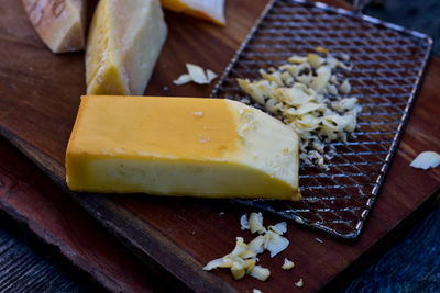 Metal cheese grater and block of smoked cheese on wood cutting board