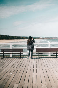 Rear view of woman sitting on pier over sea against sky