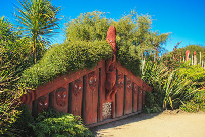 Plants and trees by house against blue sky