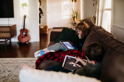 Young sister and brother using tablets at home on sick day