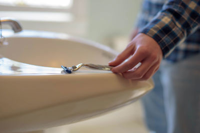 Midsection of man holding razor while standing in bathroom