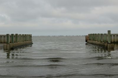 Wooden posts in sea against cloudy sky at dusk