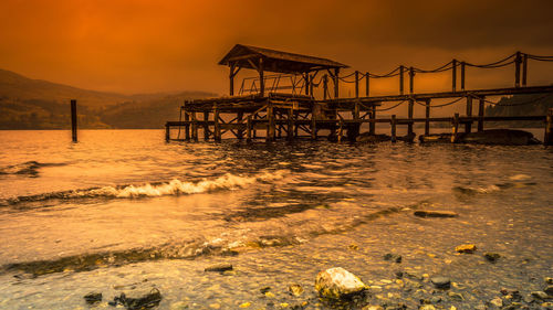 Pier on beach against sky during sunset