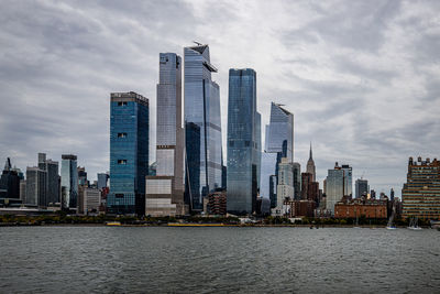 Modern buildings by river against sky in city